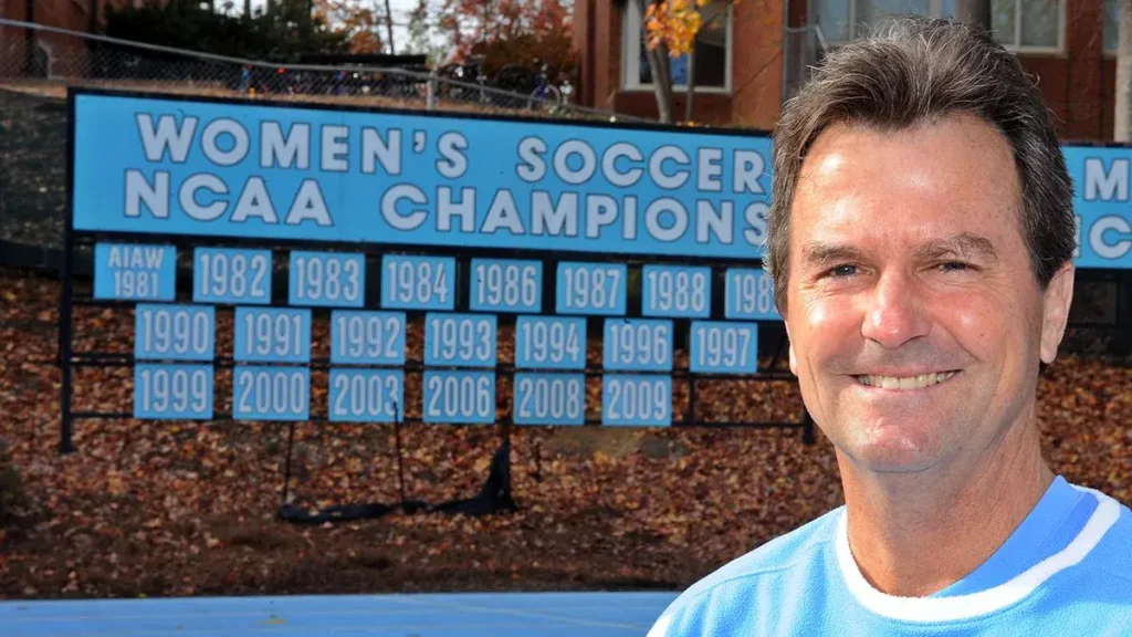 close up of anson dorrance with the ncaa championship titles in background